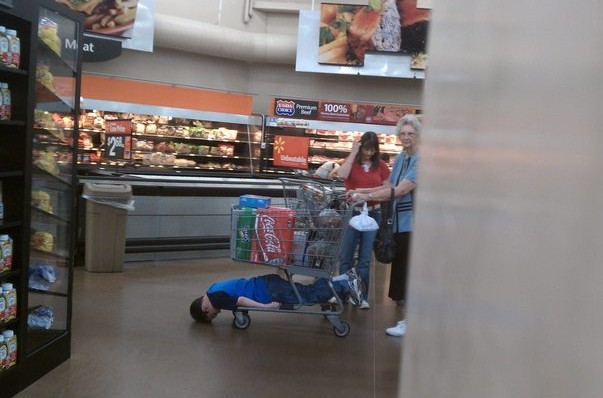 mom-takes-son-shopping-hanging-from-bottom-of-shopping-cart