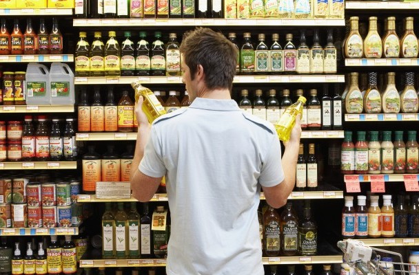 Young man in supermarket comparing bottles of oil, rear view, close-up